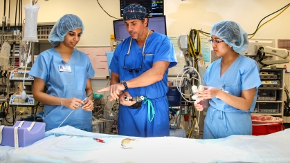 One male doctor instructing two female graduate students all wearing blue scrubs in a surgical center..