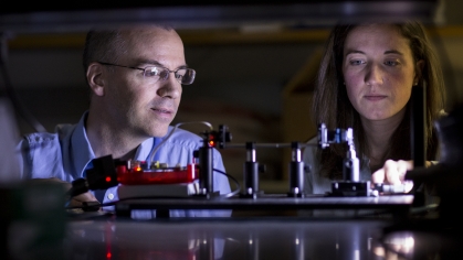 Male professor with eyeglasses working in laser laboratory with female graduate student