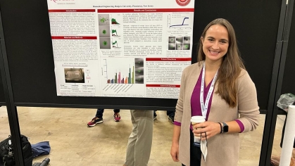 Female with long brown hair standing next to her poster presentation.