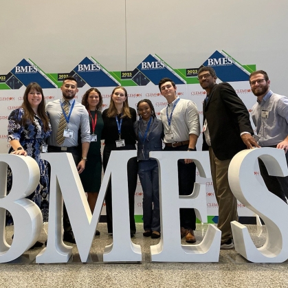 Group of students and professors standing behind a 3D BMES sign.