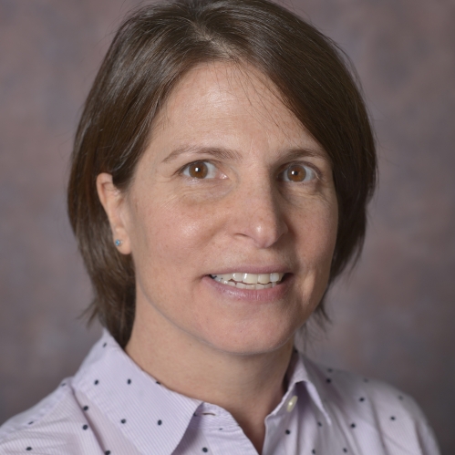 head shot of female with short brown hair wearing a light pink button down shirt with black polka dots