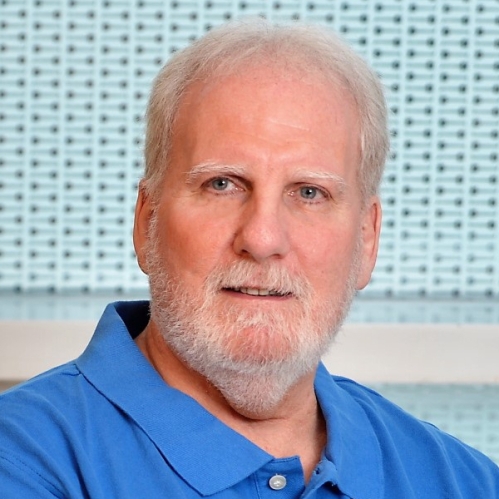 head shot of man with white hair and white beard wearing a light blue polo