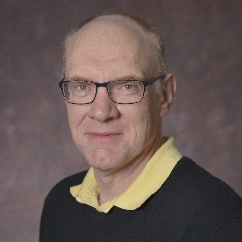 head shot of bald man with eyeglasses wearing a dark pullover sweater with a yellow collared shirt