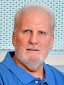 head shot of man with white hair and white beard wearing a light blue polo