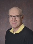 head shot of bald man with eyeglasses wearing a dark pullover sweater with a yellow collared shirt