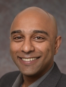 head shot of bald male  wearing a dark grey suit with grey shirt