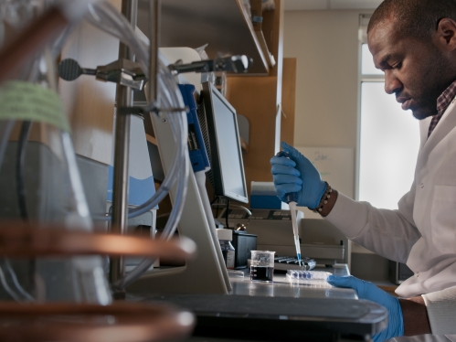 Black male graduate student conducting research with a pipette in a biomedical engineering lab. 