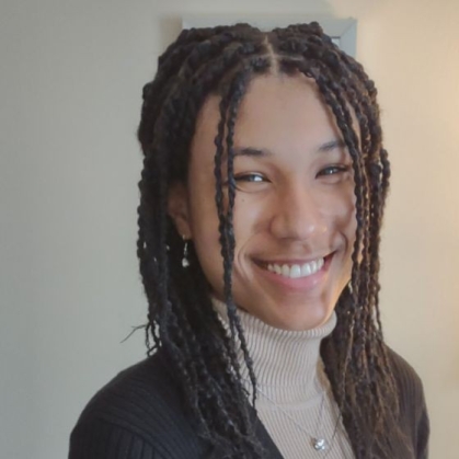 head shot of female with corn rows wearing a light brown turtle neck sweater and dark brown blazer