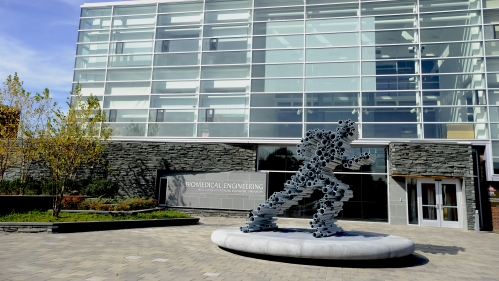 Sculpture made from pipes to mimic a running man in front of a biomedical engineering four-story building 