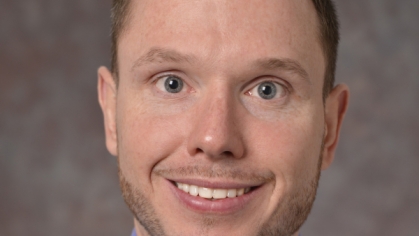 head shot of smiling male with short brown hair wearing a blue button down shirt