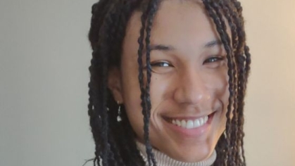 head shot of female with corn rows wearing a light brown turtle neck sweater and dark brown blazer