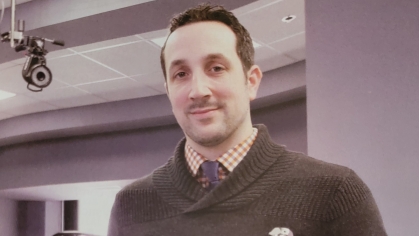 Male wearing a brown sweater with a button down shirt, holding two prosthetic devices.