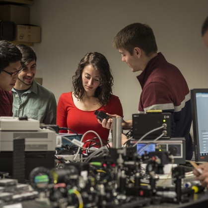 Three male students, one female student, and one male professor working in a lab.