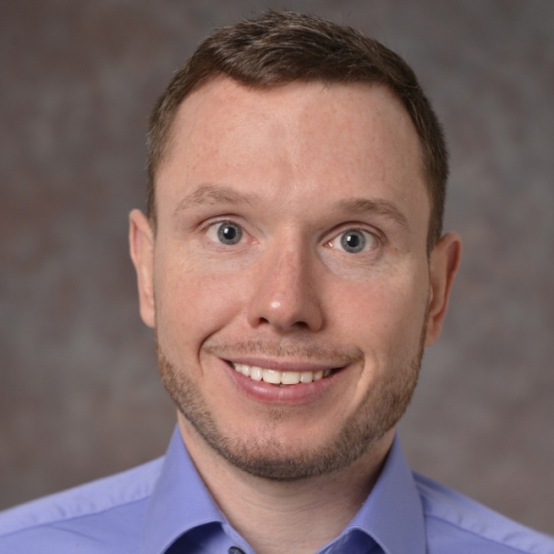 head shot of smiling male with short brown hair wearing a blue button down shirt