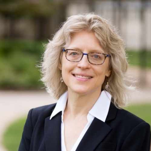 head shot of blonde woman with shoulder length hair and eyeglasses wearing a black suit jacket and white blouse with a collar