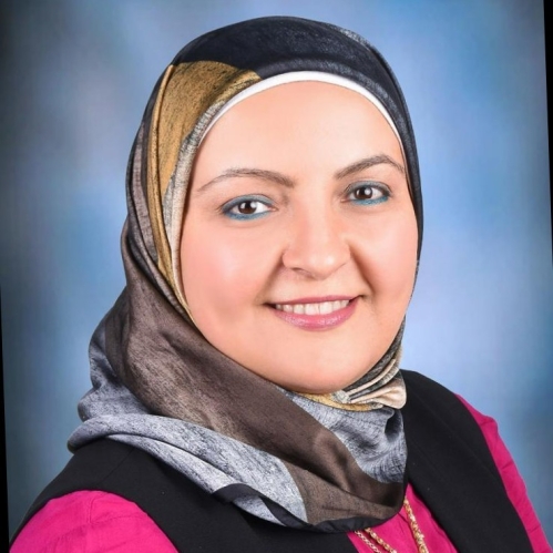 Female wearing a grey and brown head scarf, and a pink and black shirt with a necklace.