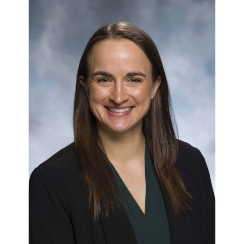 Headshot of female with long brown hair wearing a black suit jacket and dark green shirt.