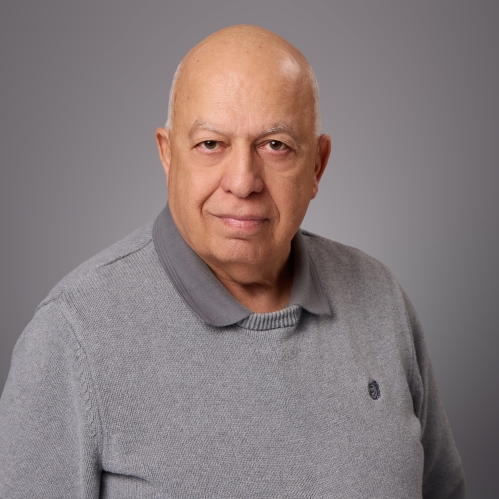 Headshot of bald male wearing a grey polo shirt underneath a grey pullover sweater.