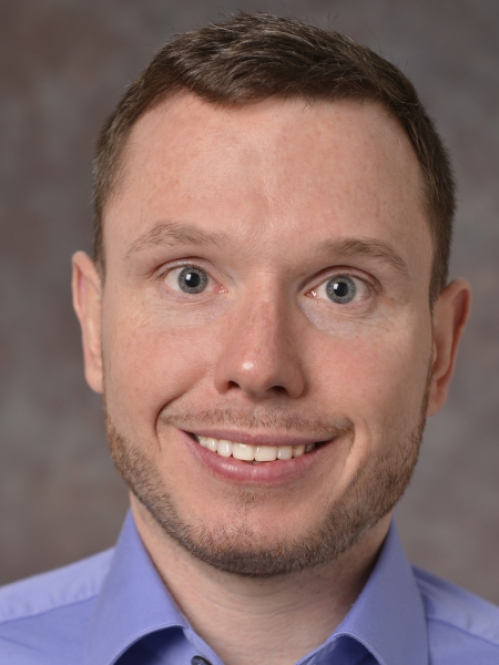 head shot of smiling male with short brown hair wearing a blue button down shirt