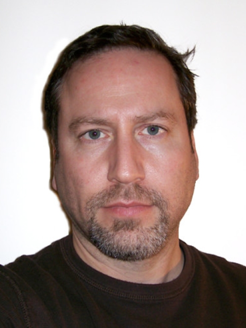 Headshot of male with short brown hair, wearing a black pullover sweater.