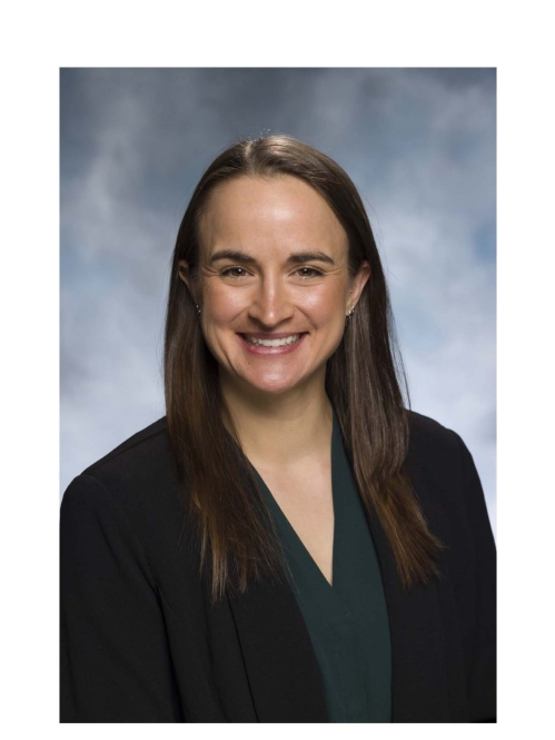 Headshot of female with long brown hair wearing a black suit jacket and dark green shirt.