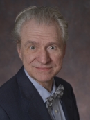 head shot of male with short grey hair wearing a dark blue suit, light blue shirt, and bow tie