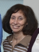 Head shot of woman with shoulder length brown hair and bangs wearing a brown and white stripped sweater.