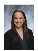 Headshot of female with long brown hair wearing a black suit jacket and dark green shirt.