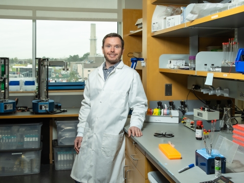 Young male professor wearing a whitle lab coat in a biomedical engineering lab.