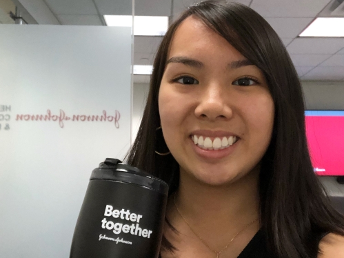 Headshot of young woman with long, black hair holding a Johnson and Johnson black travel mug that says "Better  together".