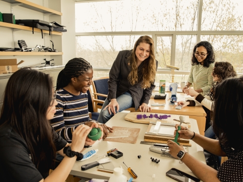 Female professor works with undergraduate students in a small conference room.