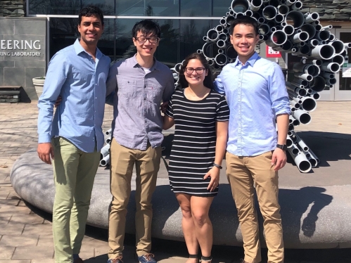 Team of three young men and one woman standing in front the the engineering sculpture and building.