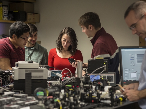 Three male students, one female student, and one male professor working in a lab.