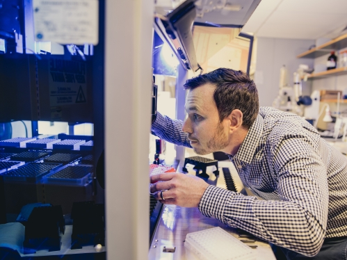 Male professor wearing a blue and white checkered shirt in a biomedical engineering lab examing the autonomous liquid handling robot.