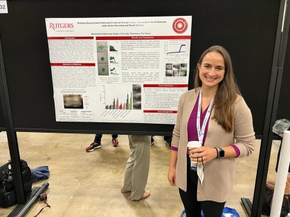 Female with long brown hair standing next to her poster presentation.