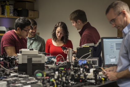 Three male students, one female student, and one male professor working in a lab.