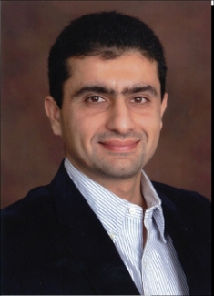 Headshot of male with short black hair wearing a black suit jacket with a white collared button down shirt.